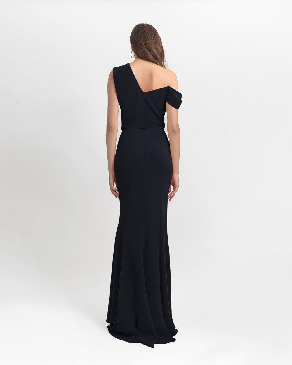 The back of an asymmetrical cut crepe long black dress with draping details on the upper part and a slim cut skirt.