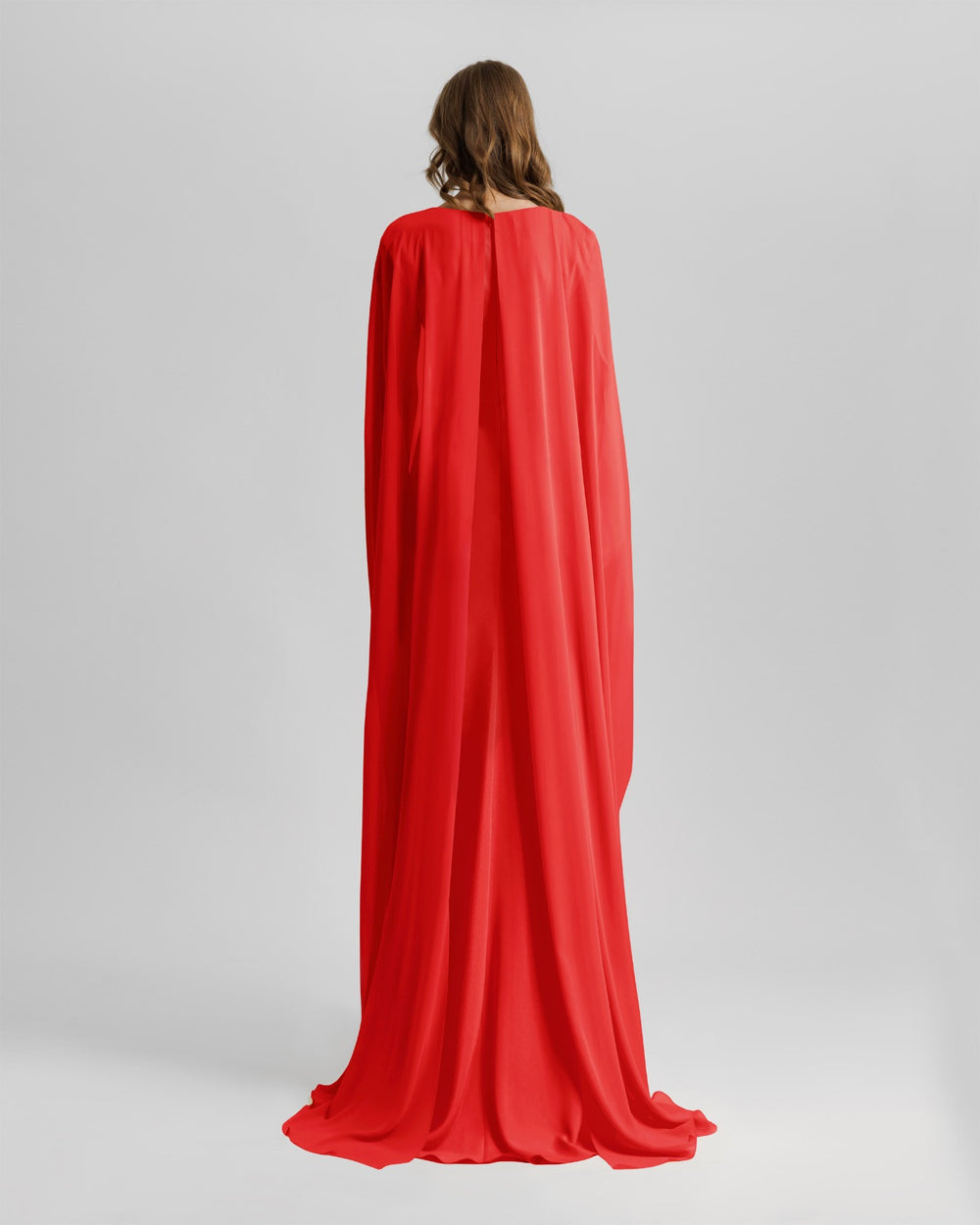 The back of a long evening red dress with cape-like draped sleeves.