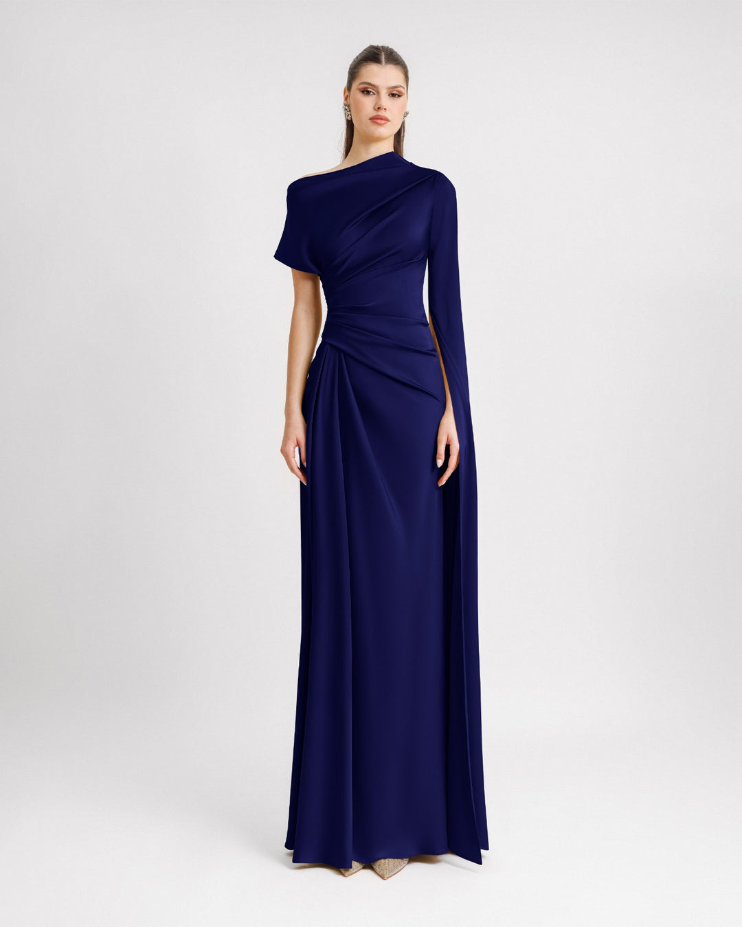 An asymmetrical neckline draped evening dress in navy blue satin fabric with a floor-length sleeve.