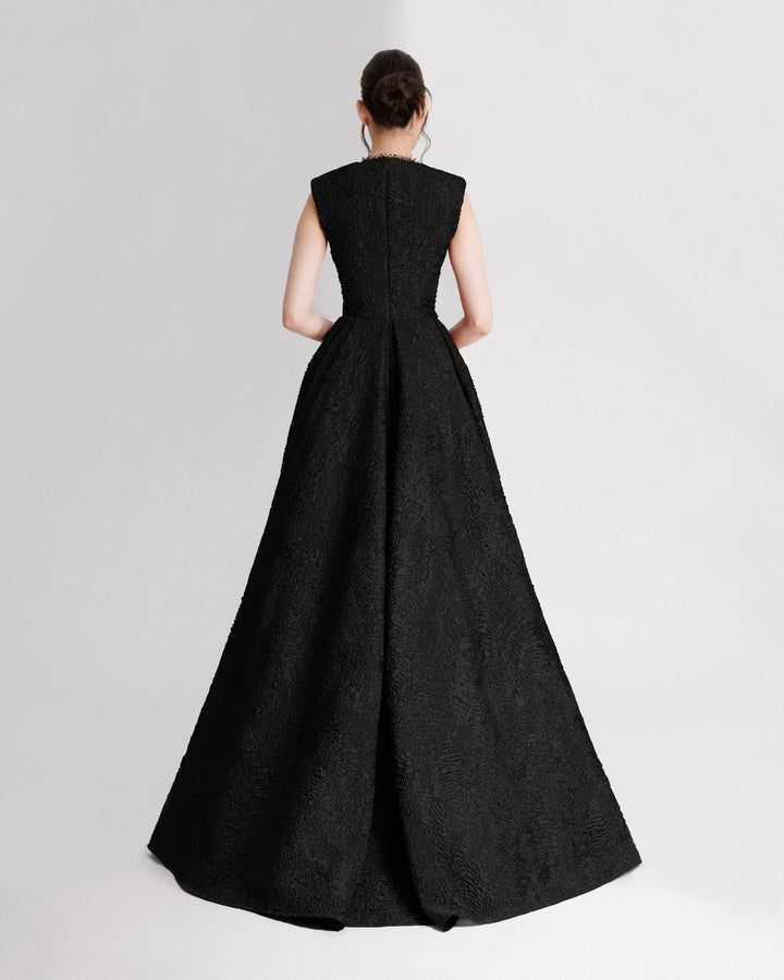 The back of a black evening dress in crinkled jacquard with structured shoulders and a draped flared skirt.