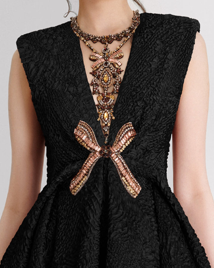 A close-up of an embellished V-neckline black dress with structured shoulders and a draped skirt.