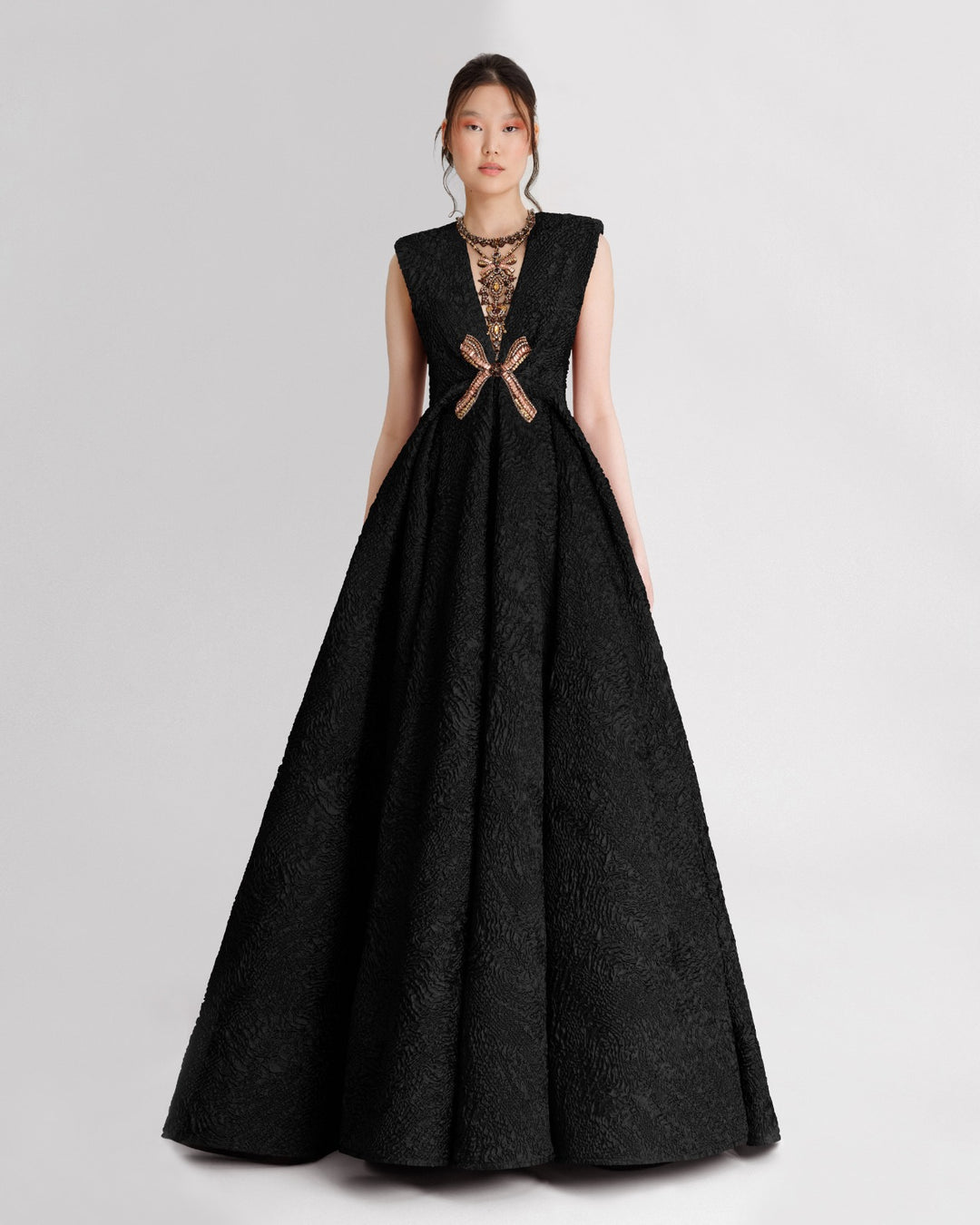 An embellished V-neckline black dress with structured shoulders and a draped flared skirt.