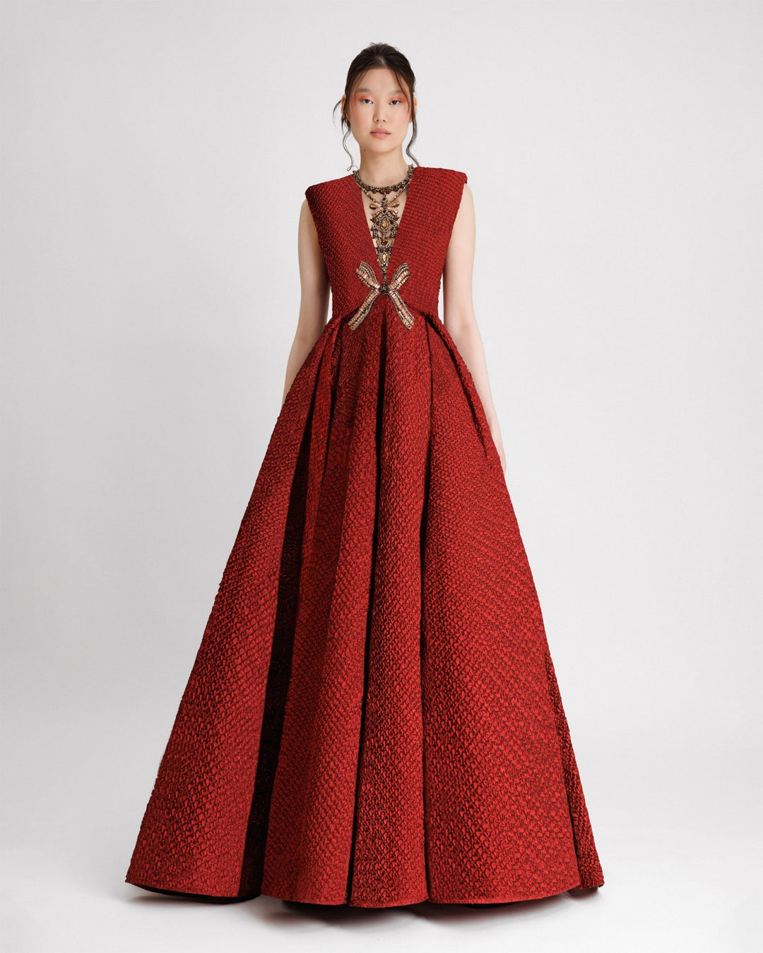 An embellished V-neckline evening dress with structured shoulders and a draped flared skirt in red crinkled jacquard fabric.