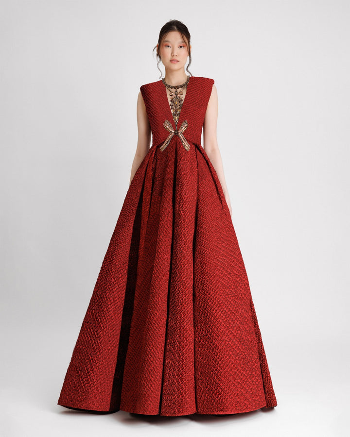 An embellished V-neckline evening dress with structured shoulders and a draped flared skirt in red crinkled jacquard fabric.