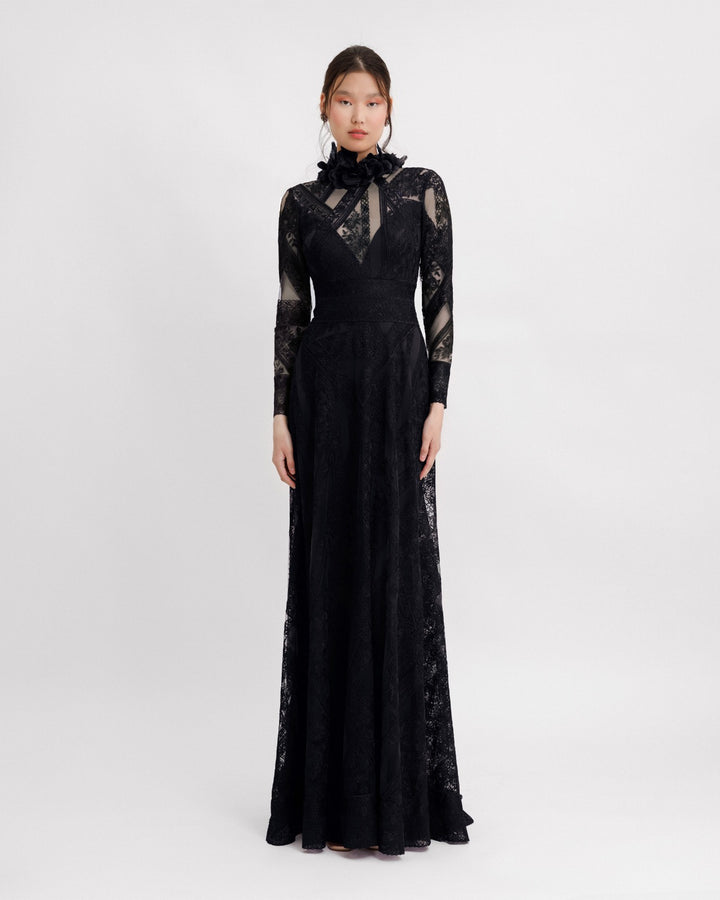 A long sleeved black dress in a patterned lace fabric, featuring a see-through plunging neckline and embroidered floral feathers on the collar.