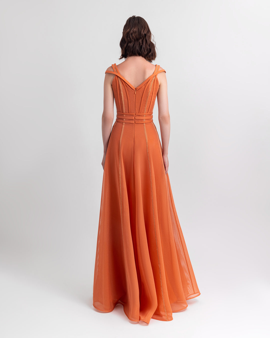 The back of a corset flared mesh orange dress with embroidery details and three stipes belt.