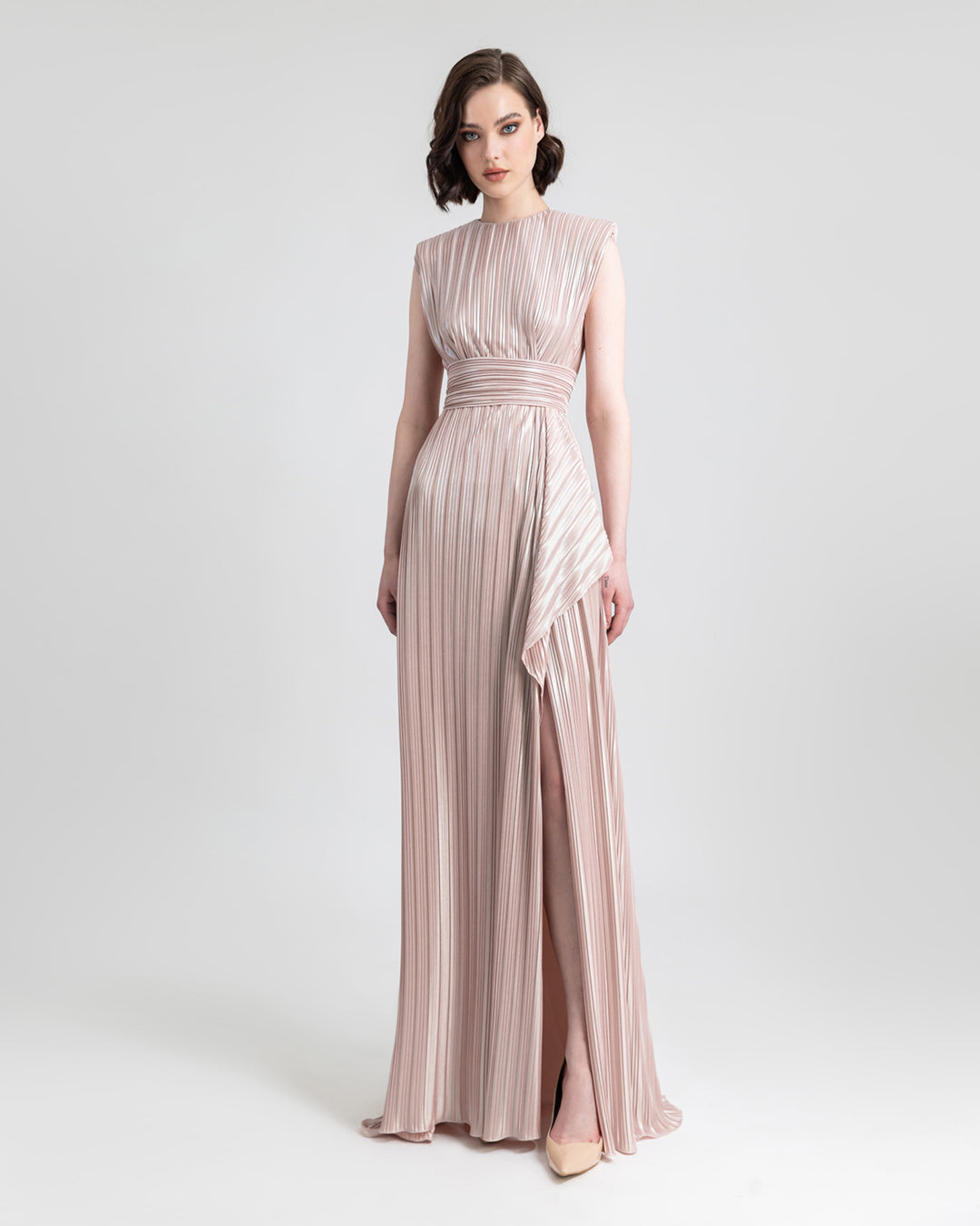 A straight cut blush evening dress with ruffles details and open slit on the side in a pleated jersey fabric.