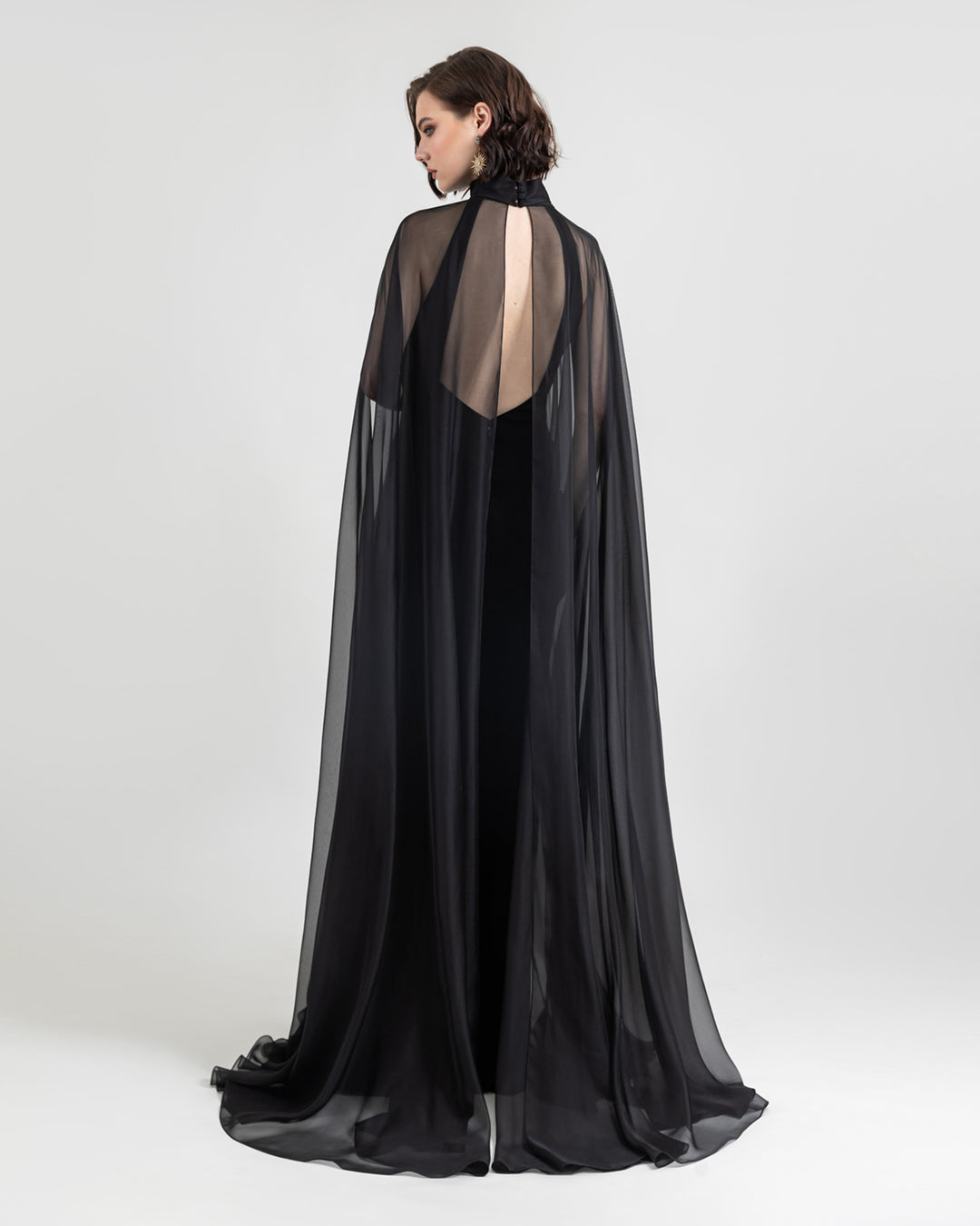 An open-back slim cut crepe long black evening dress with see through overlayered cape.