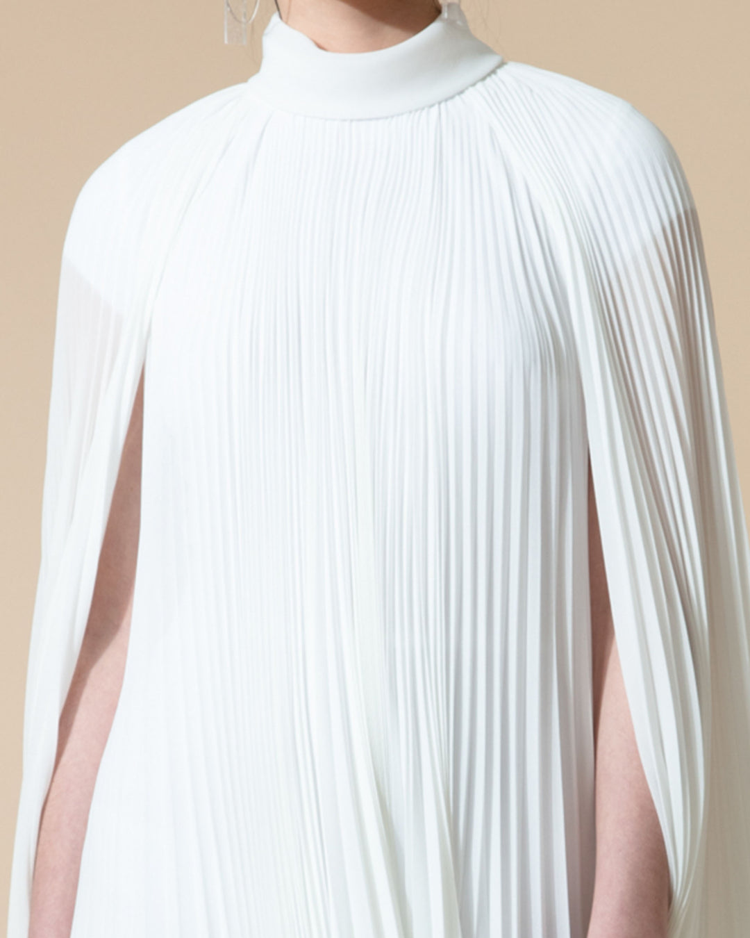 A close-up of a fully pleated flared chiffon white dress with cape-like sleeves.