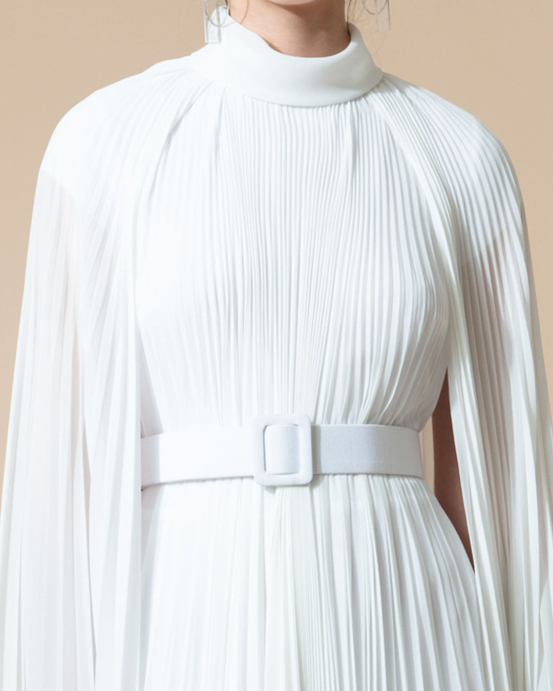 A close-up of a fully pleated flared chiffon white dress with cape-like sleeves.