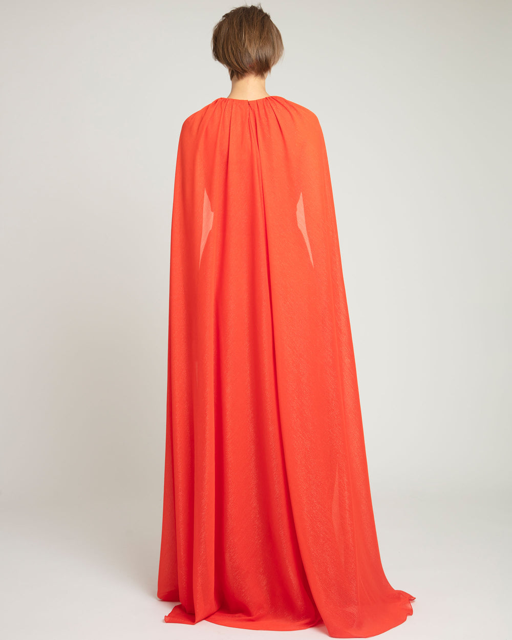 The back of a kaftan style dress in coral color featuring an overlapped cape-like sleeves.