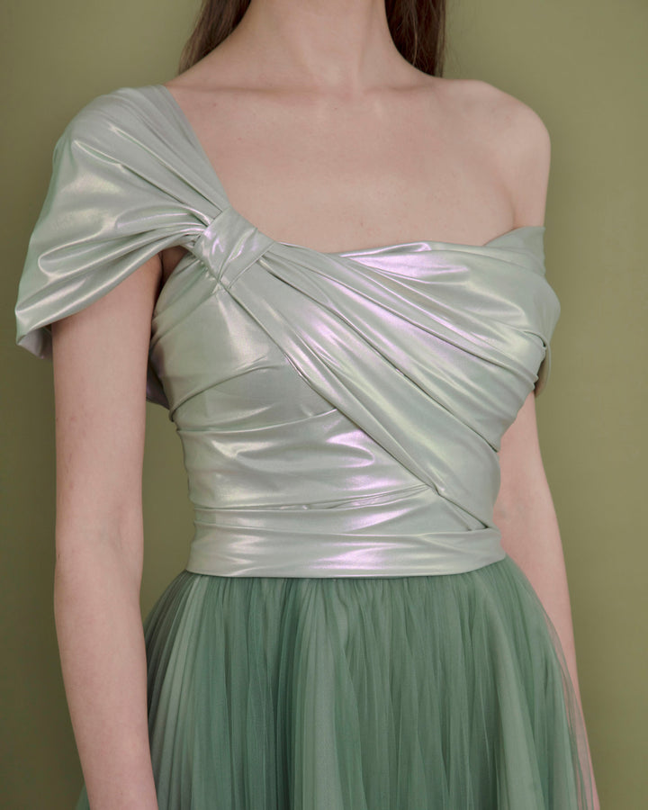 A close-up of a wide cut midi evening dress featuring an asymmetrical neckline with metallic latex bow-like design and a pleated green tulle skirt.