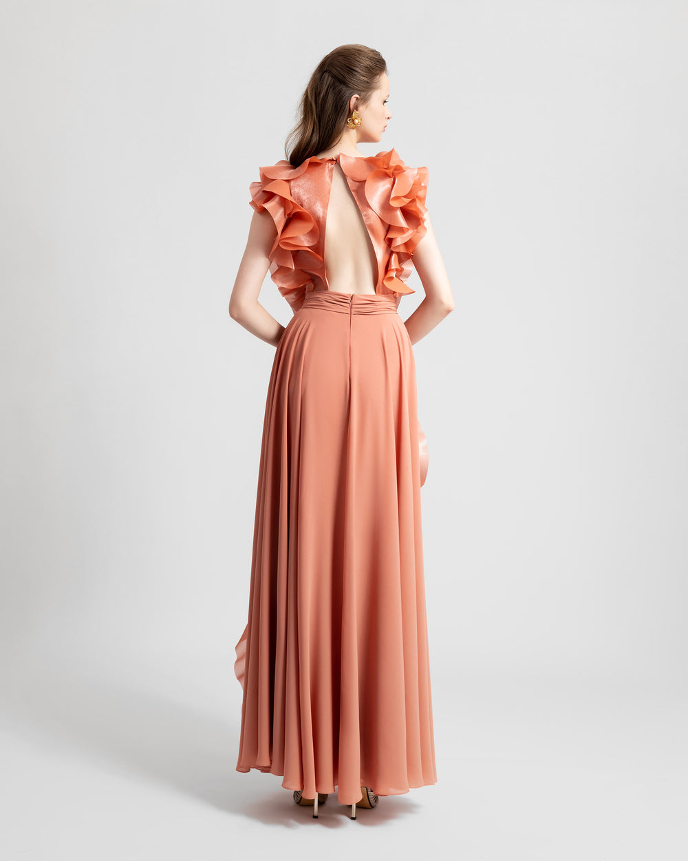 The back of a flowy crepe copper evening dress featuring an upside down v-shape open back and ruffle details on the upper sides.