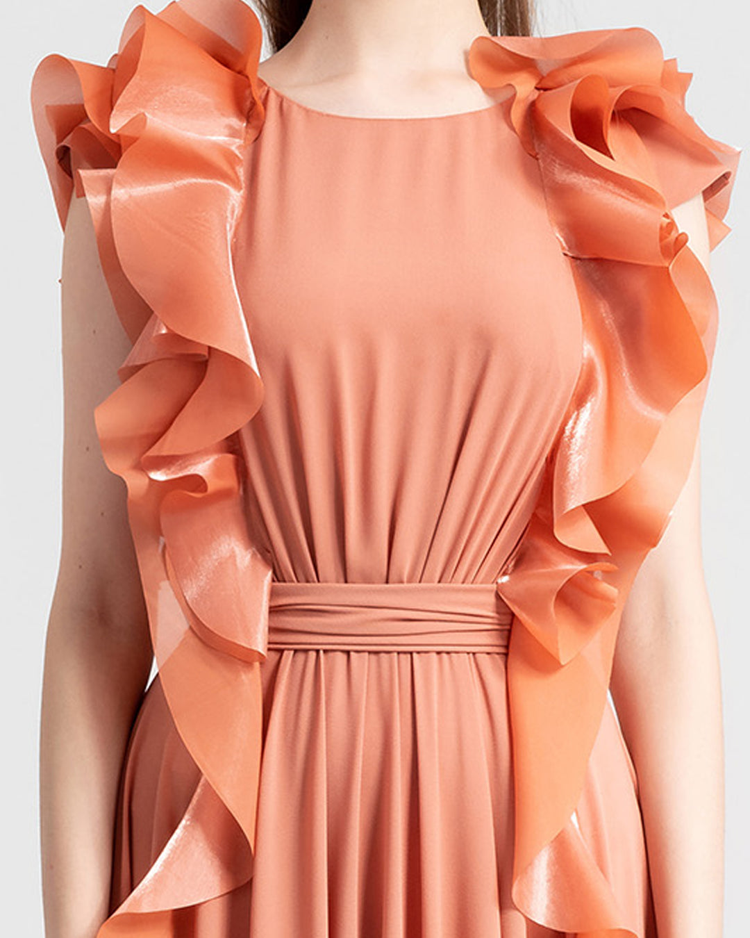 A close-up of a flowy crepe copper evening dress featuring symmetrical ruffled details on the sides from the shoulders all the way down.