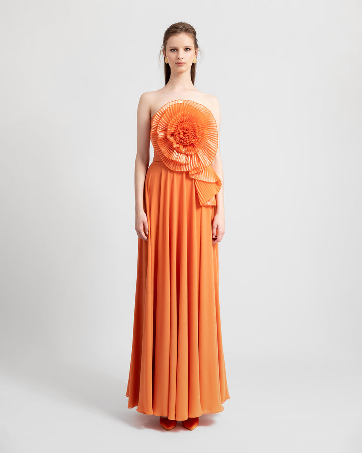 An a-cut orange strapless crepe long evening dress featuring a full bust flower design made with pleated organza fabric.