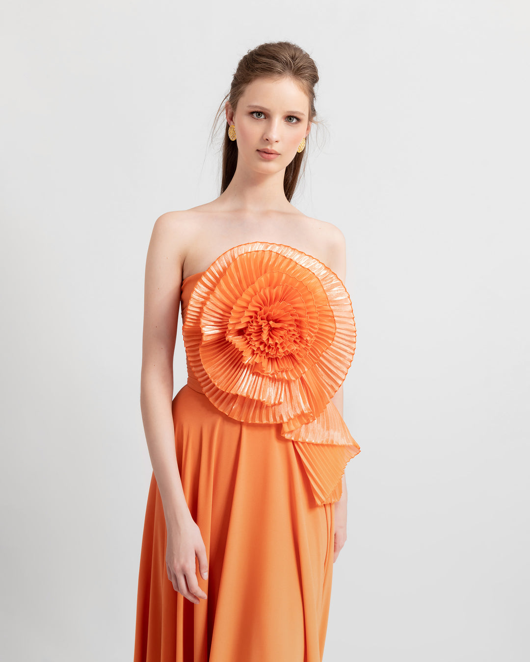 A close-up of an a-cut orange strapless crepe long evening dress featuring a full bust flower design made with pleated organza fabric.