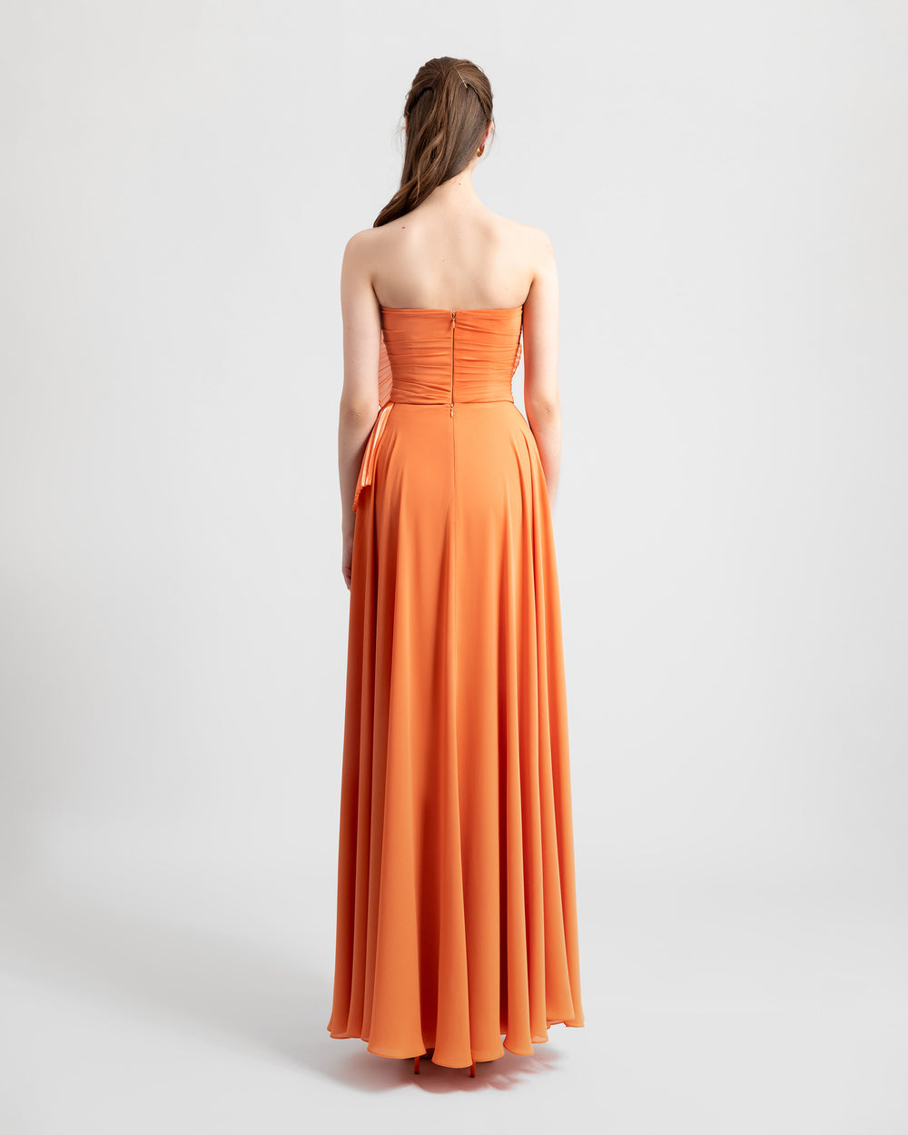 The back of an a-cut orange strapless crepe long evening dress featuring a gathered bodice design.