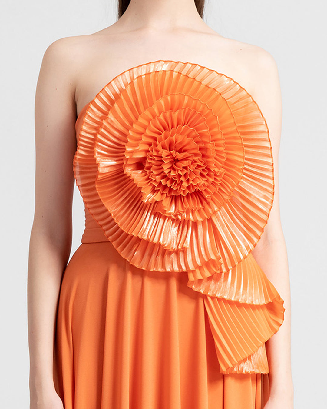 A close-up of an a-cut orange strapless crepe long evening dress featuring a full bust flower design made with pleated organza fabric.