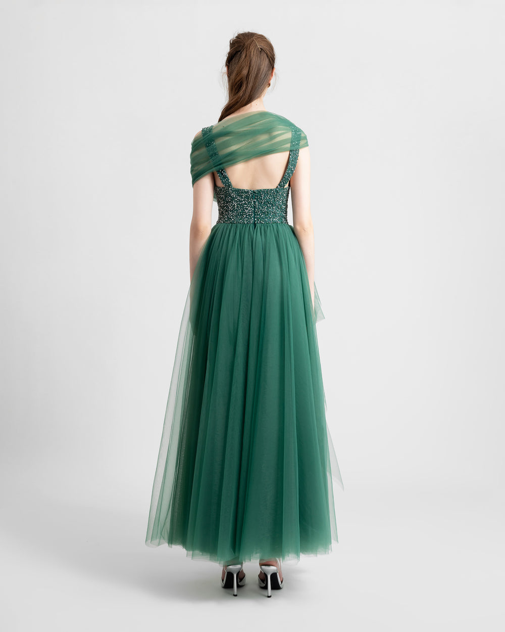 The back of a deep v-neckline a-cut green tulle evening dress with beading on the upper part and a shawl like detail.