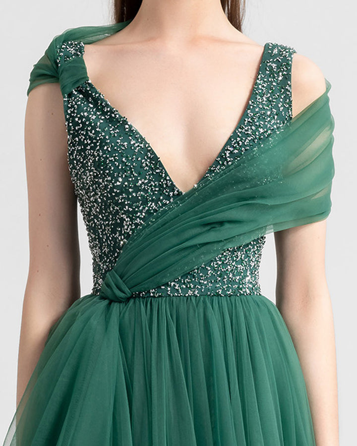 A close-up of a deep v-neckline a-cut green tulle evening dress with beading on the bust and a shawl like tulle detail.