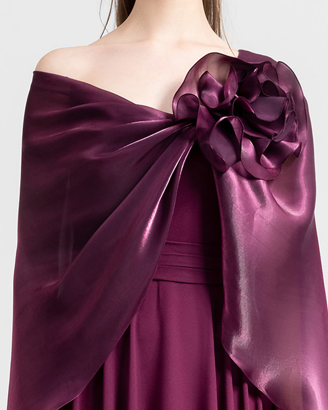 A close-up of a wide cut neckline with an embellished flower and cape-like sleeves flared soft lame organza evening dress in burgundy color.