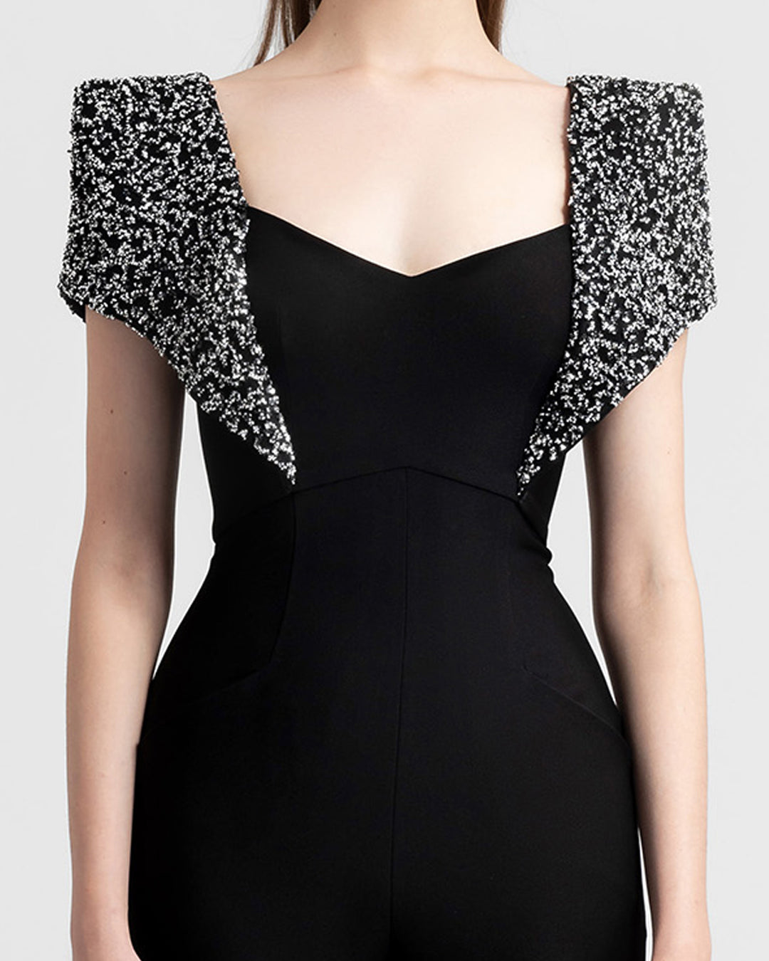 A close-up of a straight-cut black crepe jumpsuit featuring fully beaded shoulders.