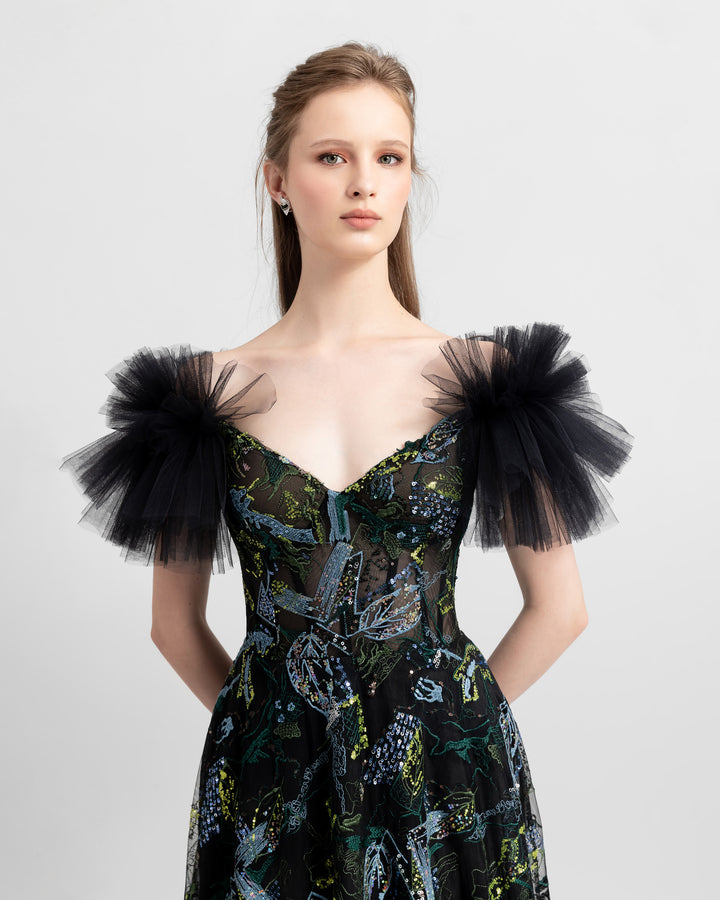 A close-up  of a slightly off-shoulders with ruched tulle sleeves black evening dress, made of fully embroidered tulle and featuring a see-through bodice.