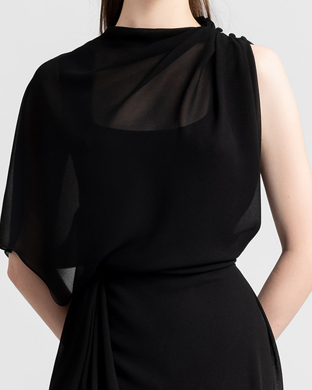 A close-up of an asymmetrical chiffon black dress with one sleeve and draping details.