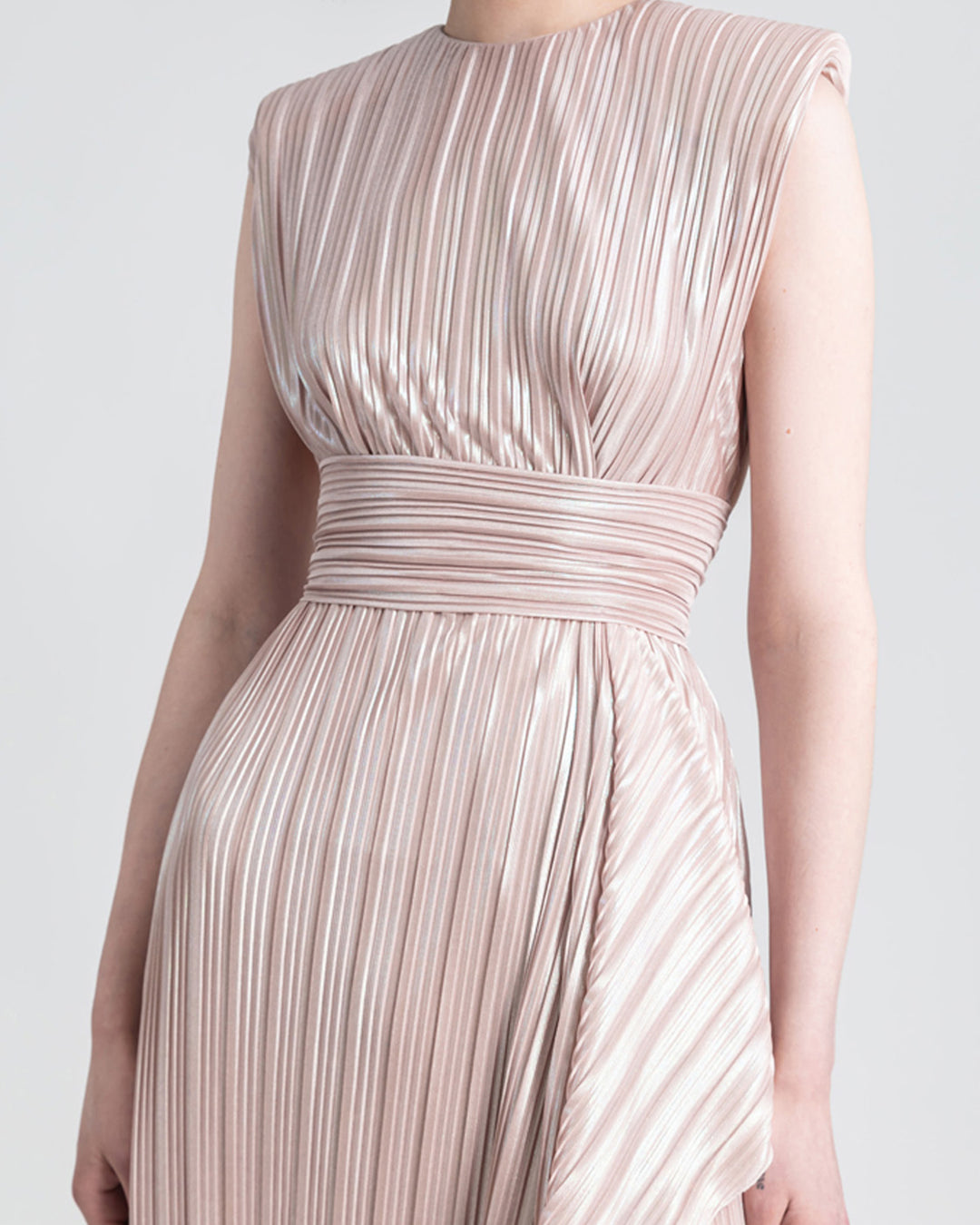 A close-up of a straight cut blush evening dress with ruffles details and open slit on the side in a pleated jersey fabric.