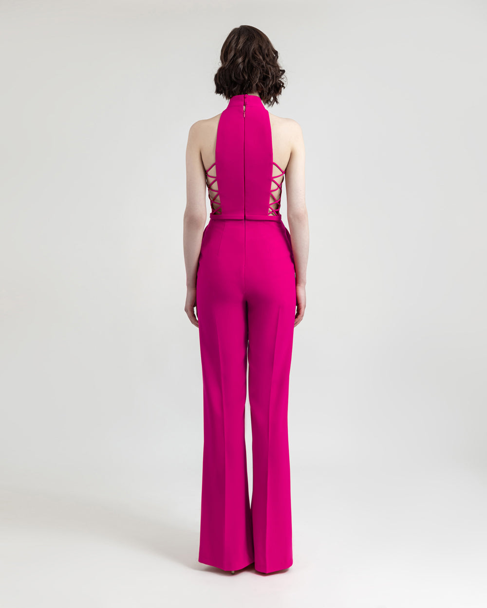 The back of a halter-cut neckline fuchsia jumpsuit with side cut-out details and flared cut pants.