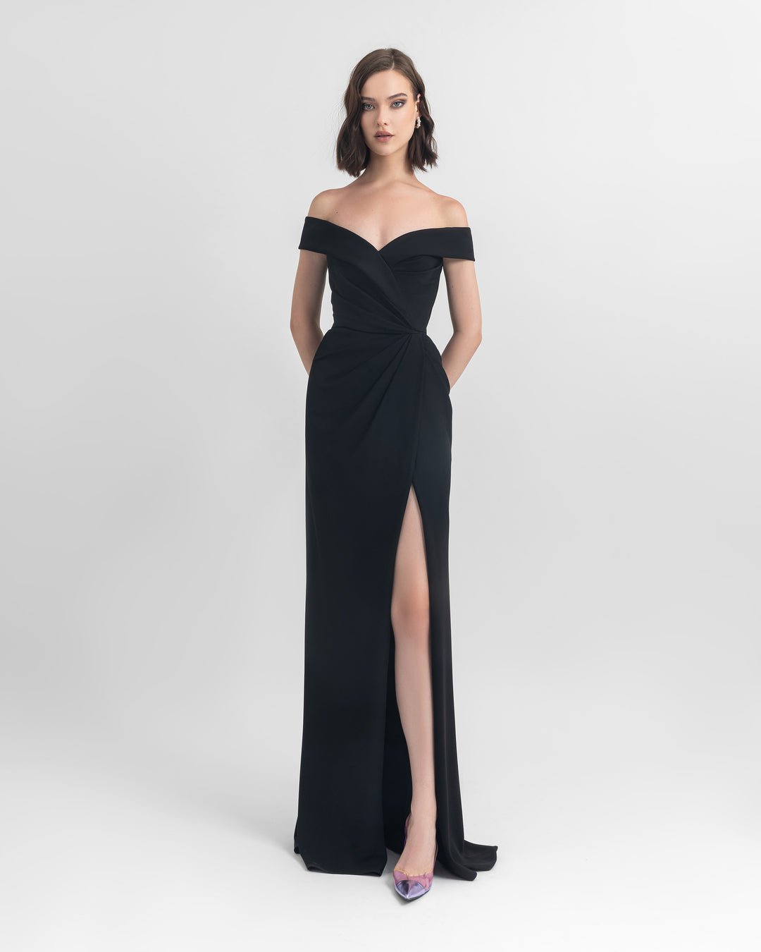 An off-shoulder slim cut crepe long black dress with draping details on the waist and an open slit on the side.