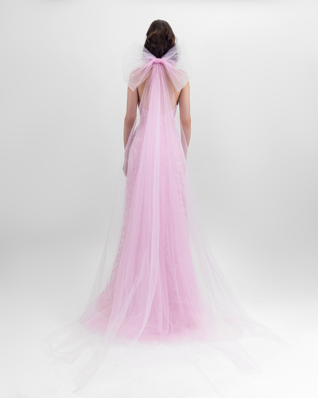 The back of a flared cut long pink dress with a backless design, paired with a detachable tulle cape.