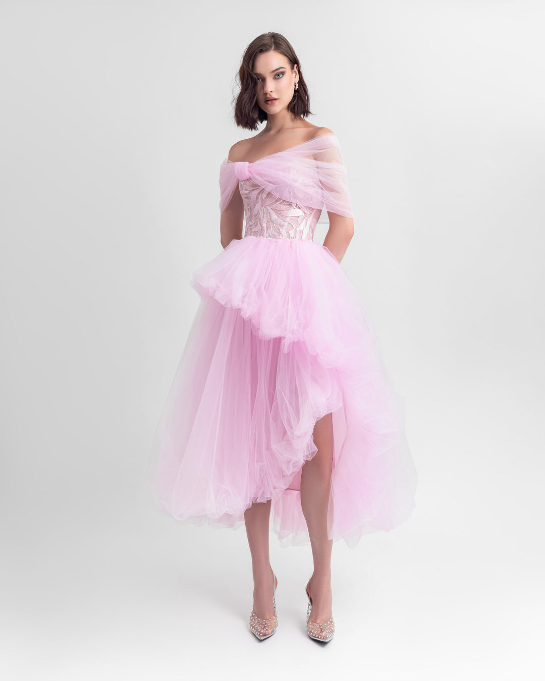 A bow-like off-shoulder cut tulle dress in pink with an embroidered corset and an asymmetrical ruffled skirt.