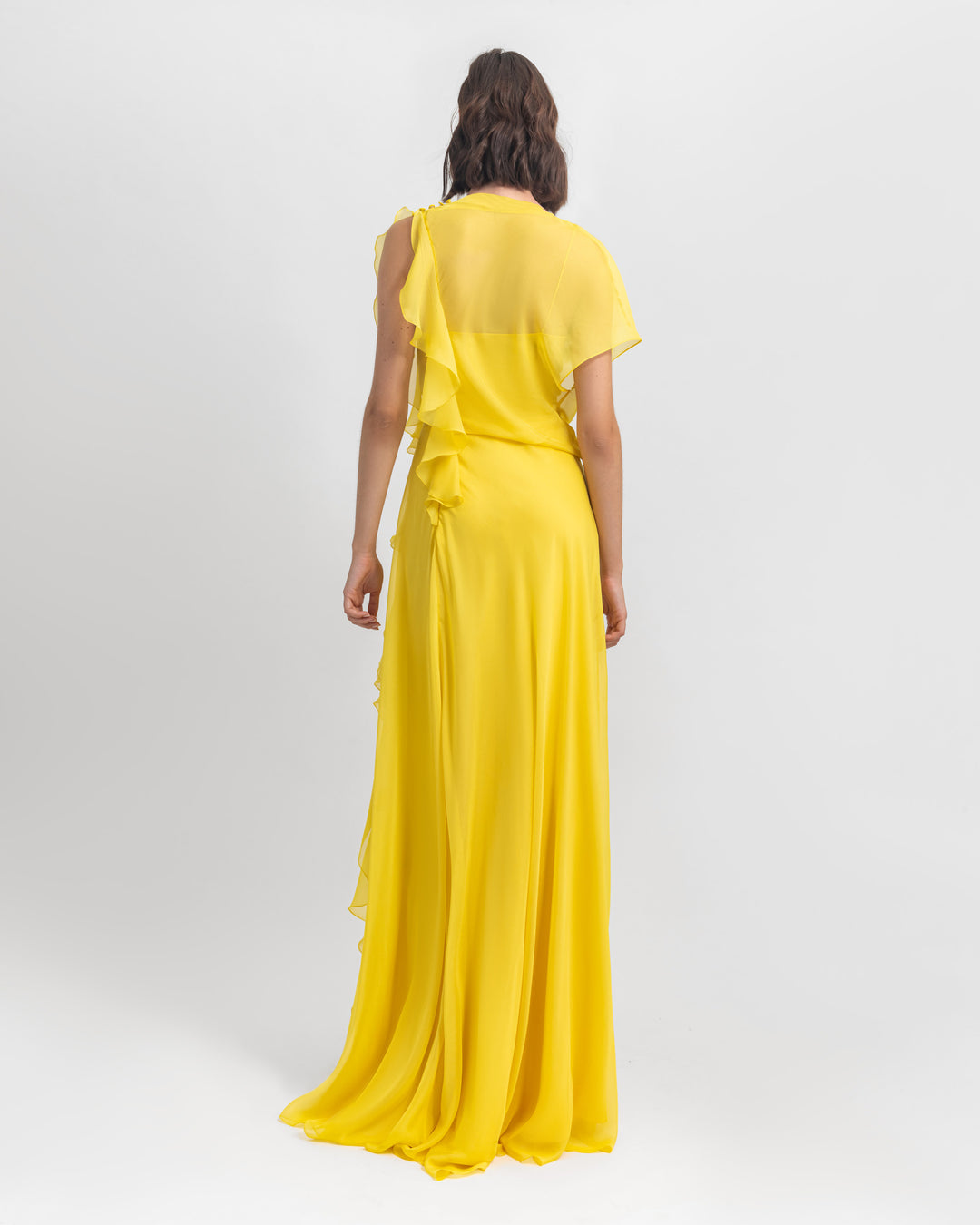 The back of an asymmetrical flared chiffon yellow dress with draping and ruffled details.