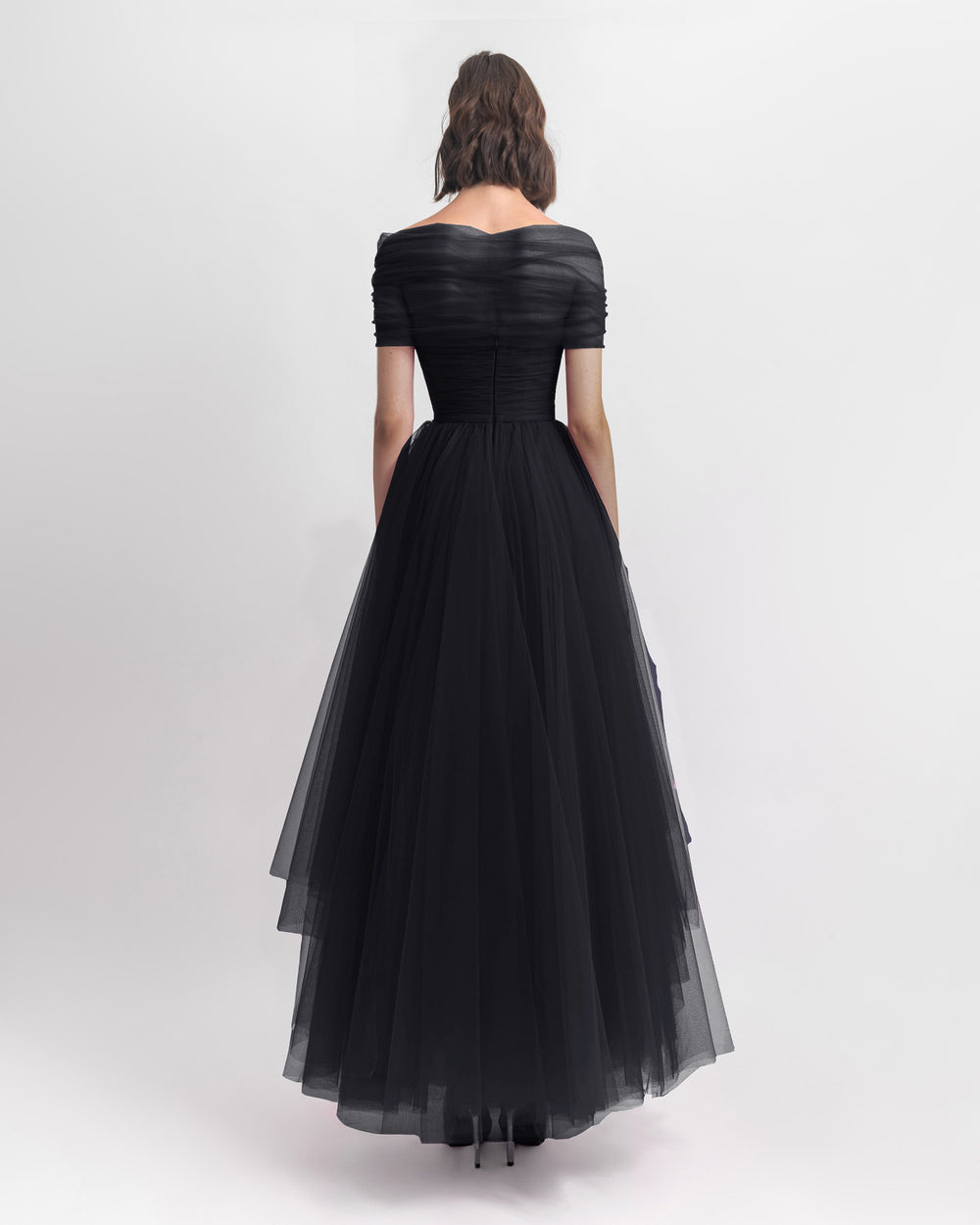 The back of an off-shoulder black tulle dress with an asymmetrical lower part.