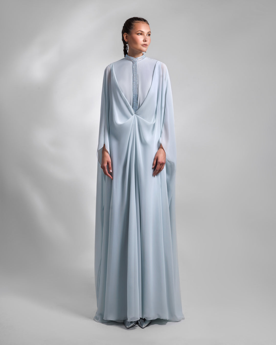 A long loose chiffon blue evening dress with draping and embellishment details.