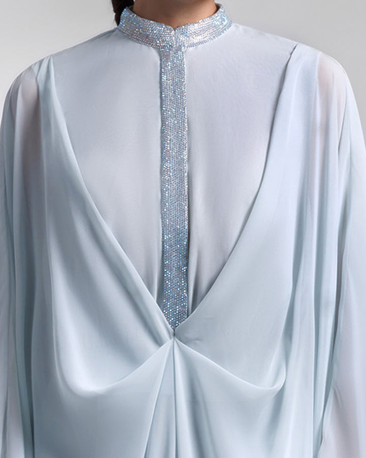 A close-up of a loose chiffon blue evening dress with draping and embellishment details.