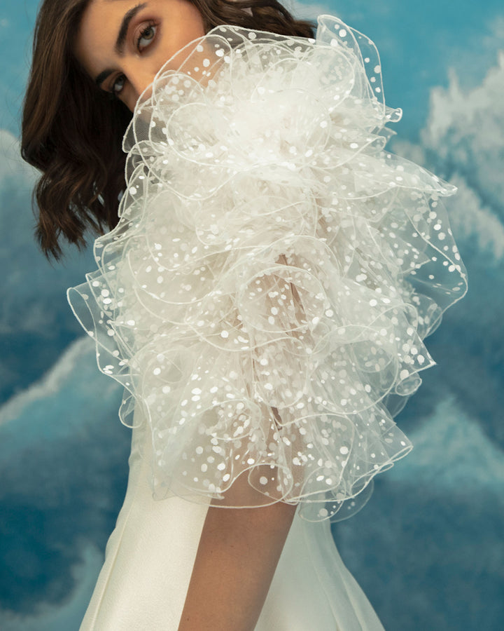 A close-up of a princess cut ivory short dress, comes in a jacquard fabric featuring dramatical ruffled shoulders.