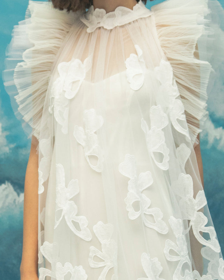 A close-up of an A-line cut white midi dress in fully embroidered fabric, featuring ruffled shoulders.