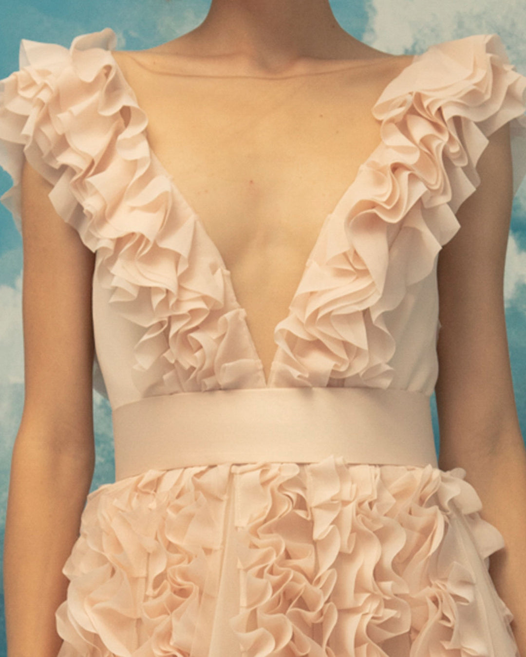 A close-up of a deep V-neckline, fully ruffled flared evening dress with laser-cut chiffon on tulle fabric.