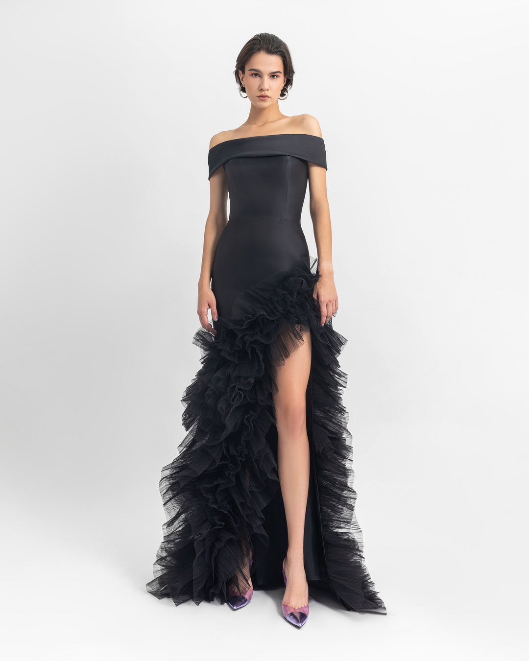 An off-shoulder satin long black dress with an open slit on the side and ruffled tulle details.