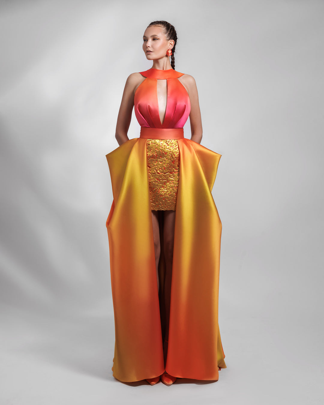 A deep V-neckline heavy satin dress in orange, fuchsia and yellow hues, featuring an intricated laser cut skirt, with a symmetrical pleated overskirt.