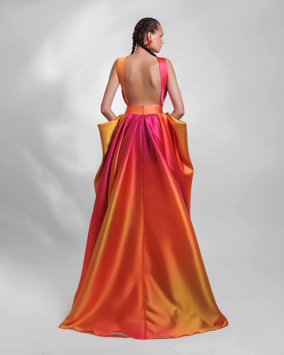 An open-back heavy satin evening dress in orange, yellow, and fuchsia hues, with pleating details and symmetrical draped details on the side.