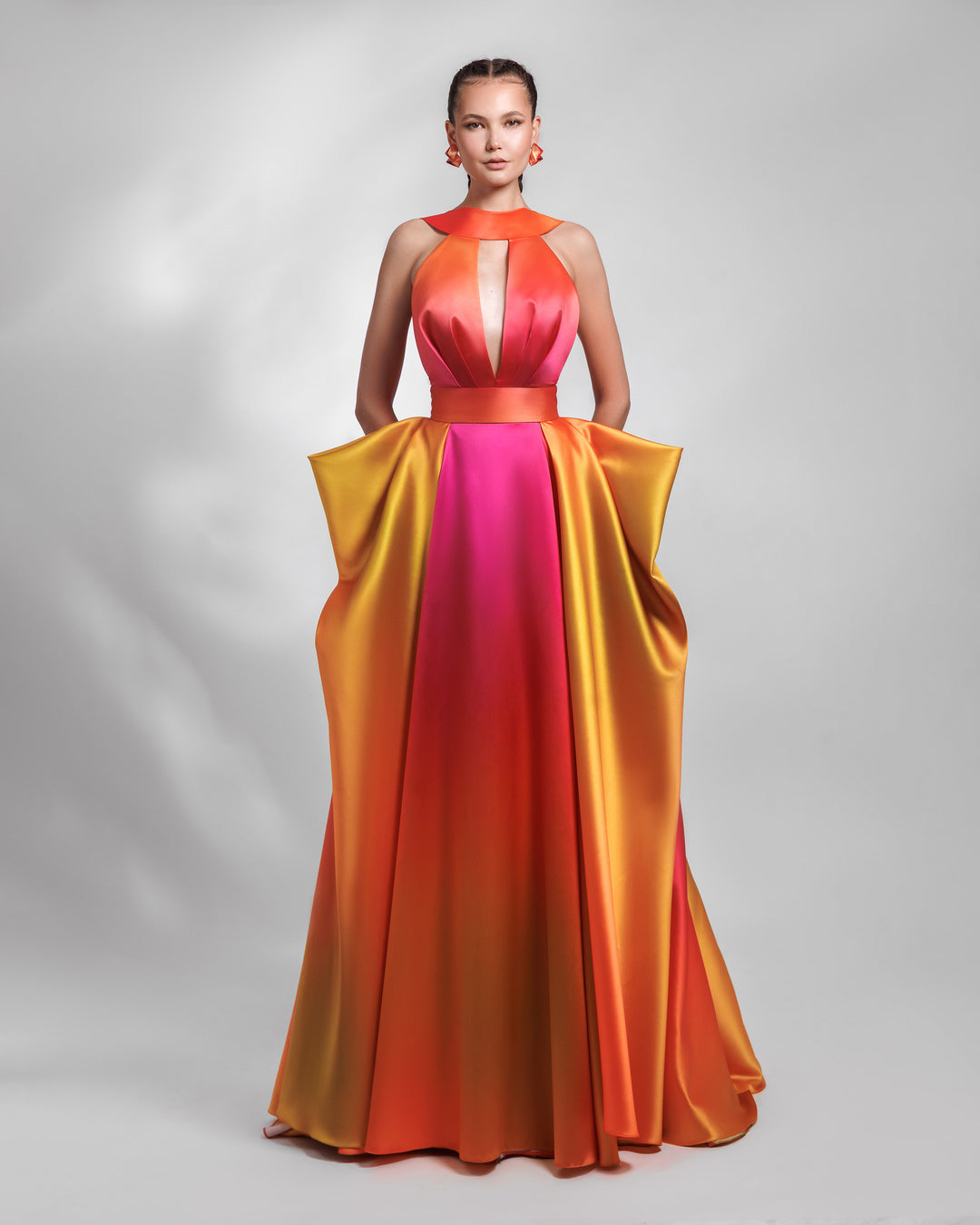 A deep V-neckline long heavy satin evening dress in orange, yellow, and fuchsia hues, with pleating details and symmetrical draped details on the side.