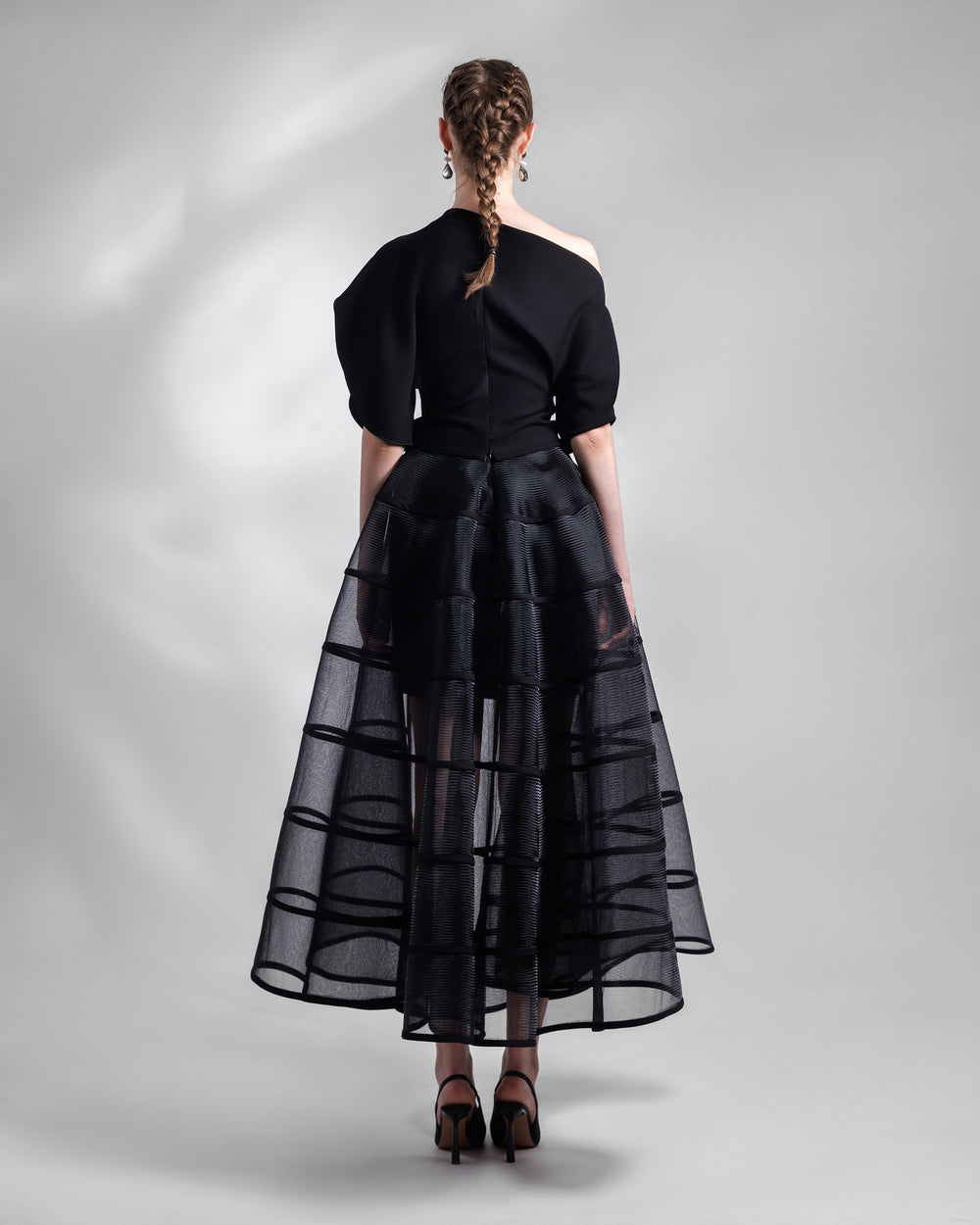 The back of a black evening wear set featuring an asymmetrical draped crepe top with slit on the sleeves, matched with a cage-like skirt.