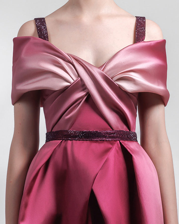 A close-up of a heavy satin midi dress in pink and burgundy hues, with a bow-like draped bodice, beaded straps and belt, and a pleated skirt.