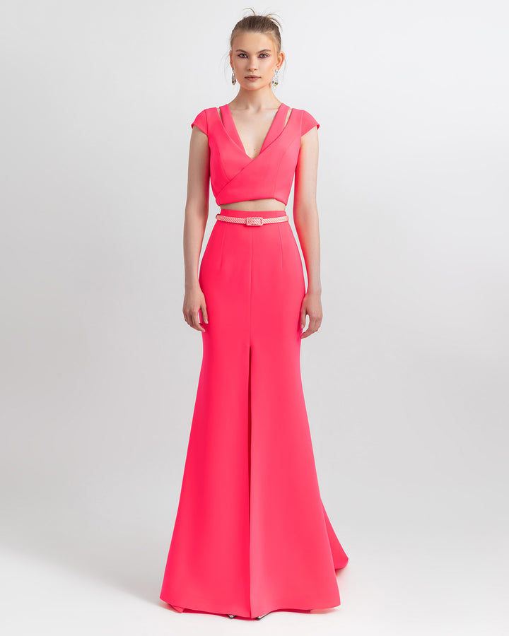 A modern evening wear style featuring a pink cropped top with cut out details, paired with a flowing mermaid-cut skirt and a detachable belt.