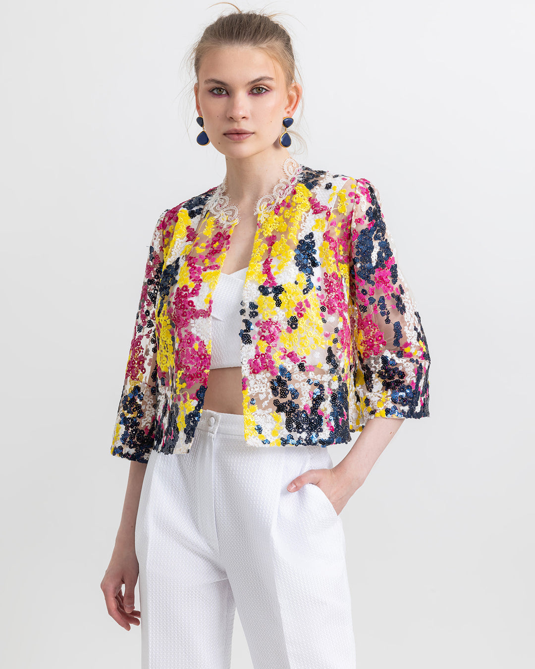 A close-up of an occasion wear featuring a white cropped top paired with a multicolor sequined jacket and a cigarette cut white pants.