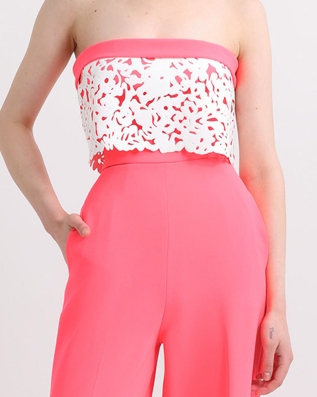 A close-up of an occasion wear featuring a strapless neon pink top with white laser-cut silicon details matched with a straight cut pants in neon pink.