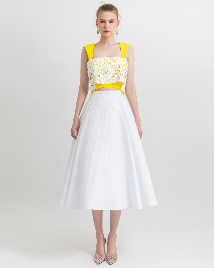 A modern outfit featuring a yellow and white laser cut cropped top paired with w full white flared skirt.